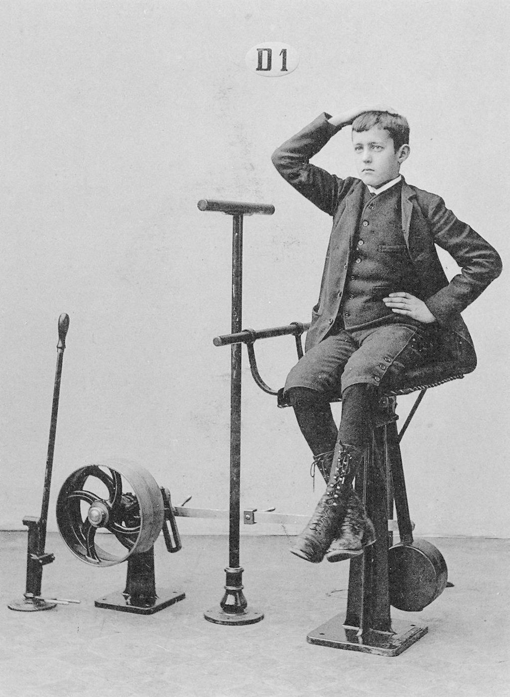 A vintage black and white photograph of a young boy posing with a collection of unusual exercise equipment.