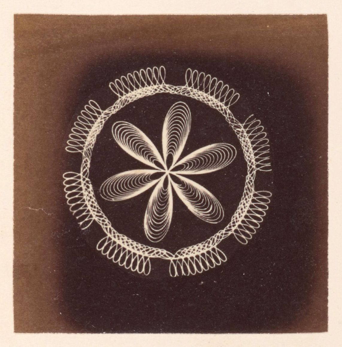 Vintage photograph of a complex geometric pattern resembling a flower surrounded by spirals.