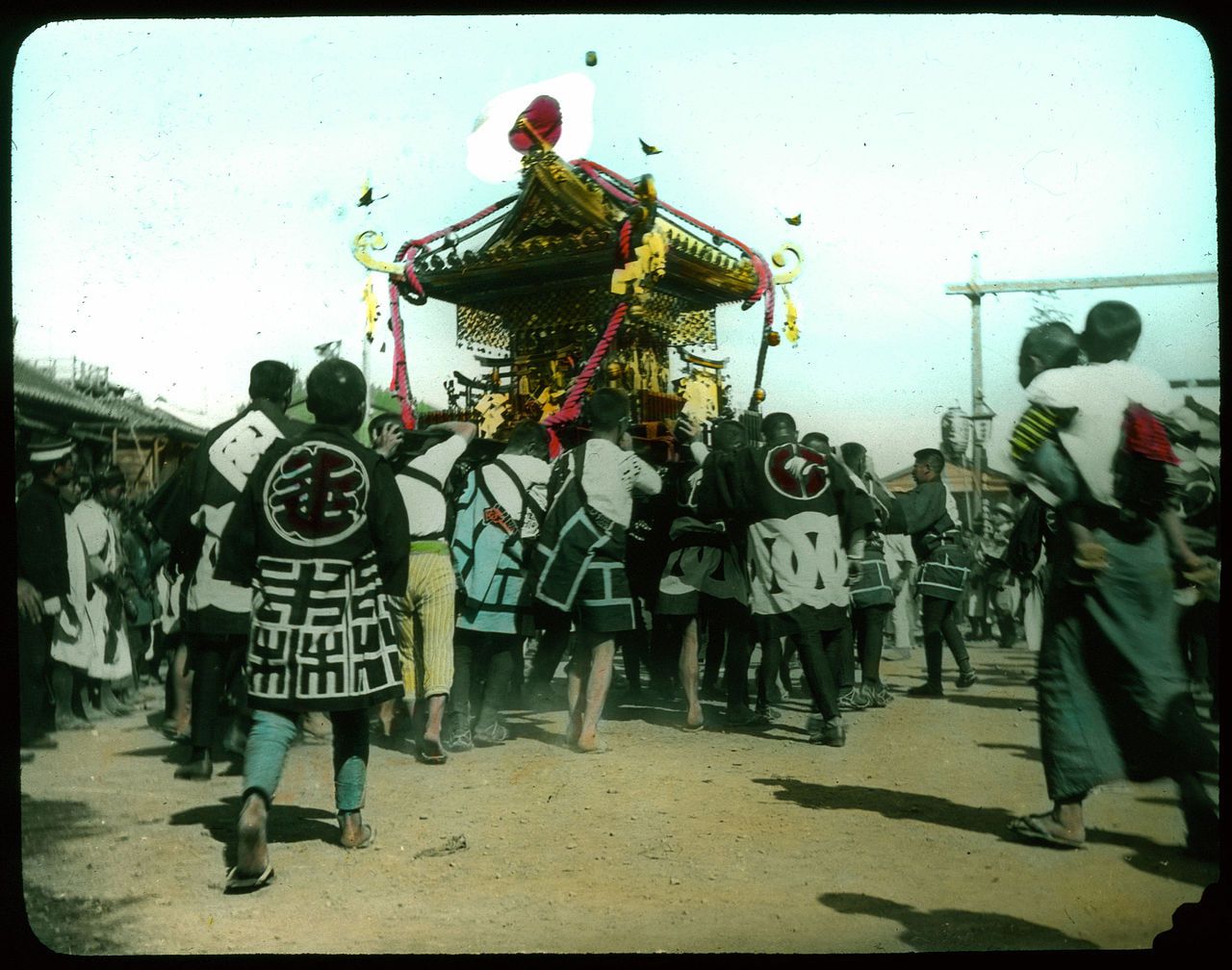 A vibrant and culturally rich outdoor scene, likely a traditional procession or event. A large, ornate platform is being carried by a group of people, creating a focal point in the image.