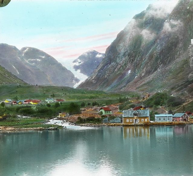 Vintage colorized photograph of a fjord landscape with mountains, a village, and a glacier.