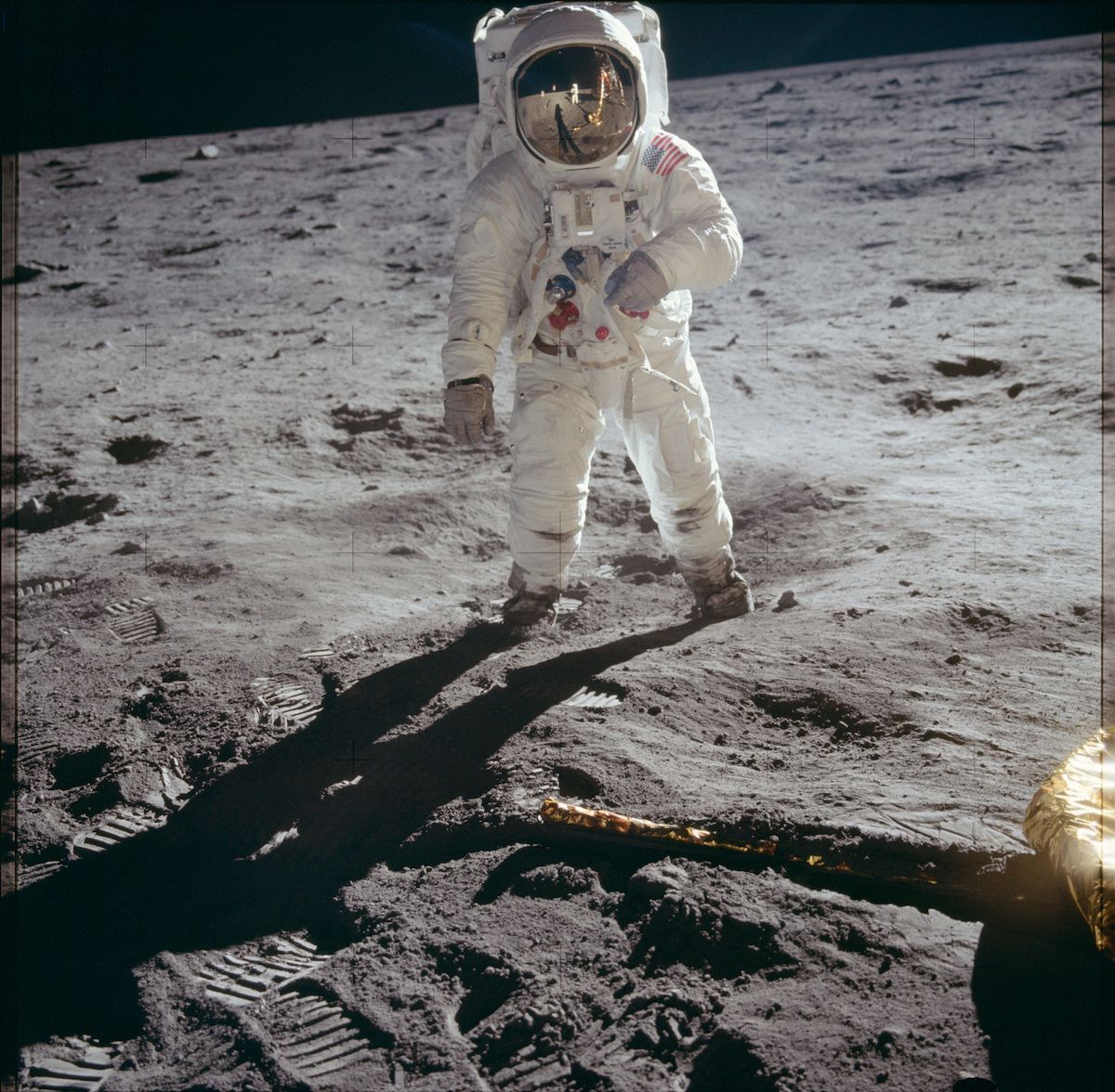 An astronaut stands on the moon, leaving footprints in the gray dust. A long shadow stretches behind them, and the dark sky is visible in the background.