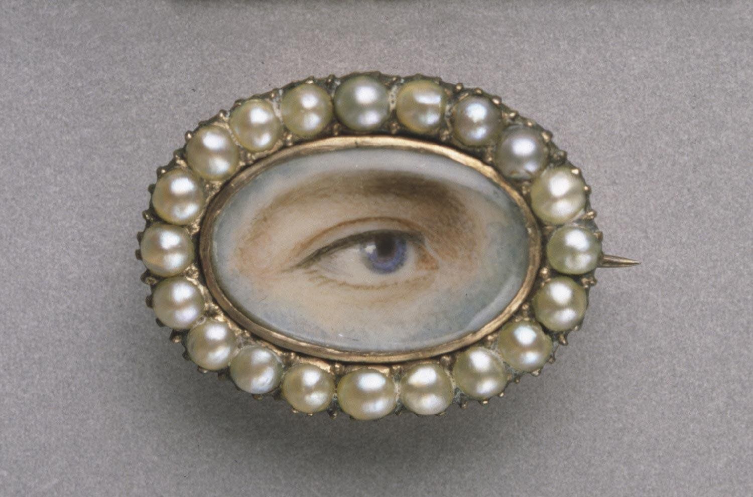 Close-up of a vintage brooch featuring a painted eye surrounded by pearls.