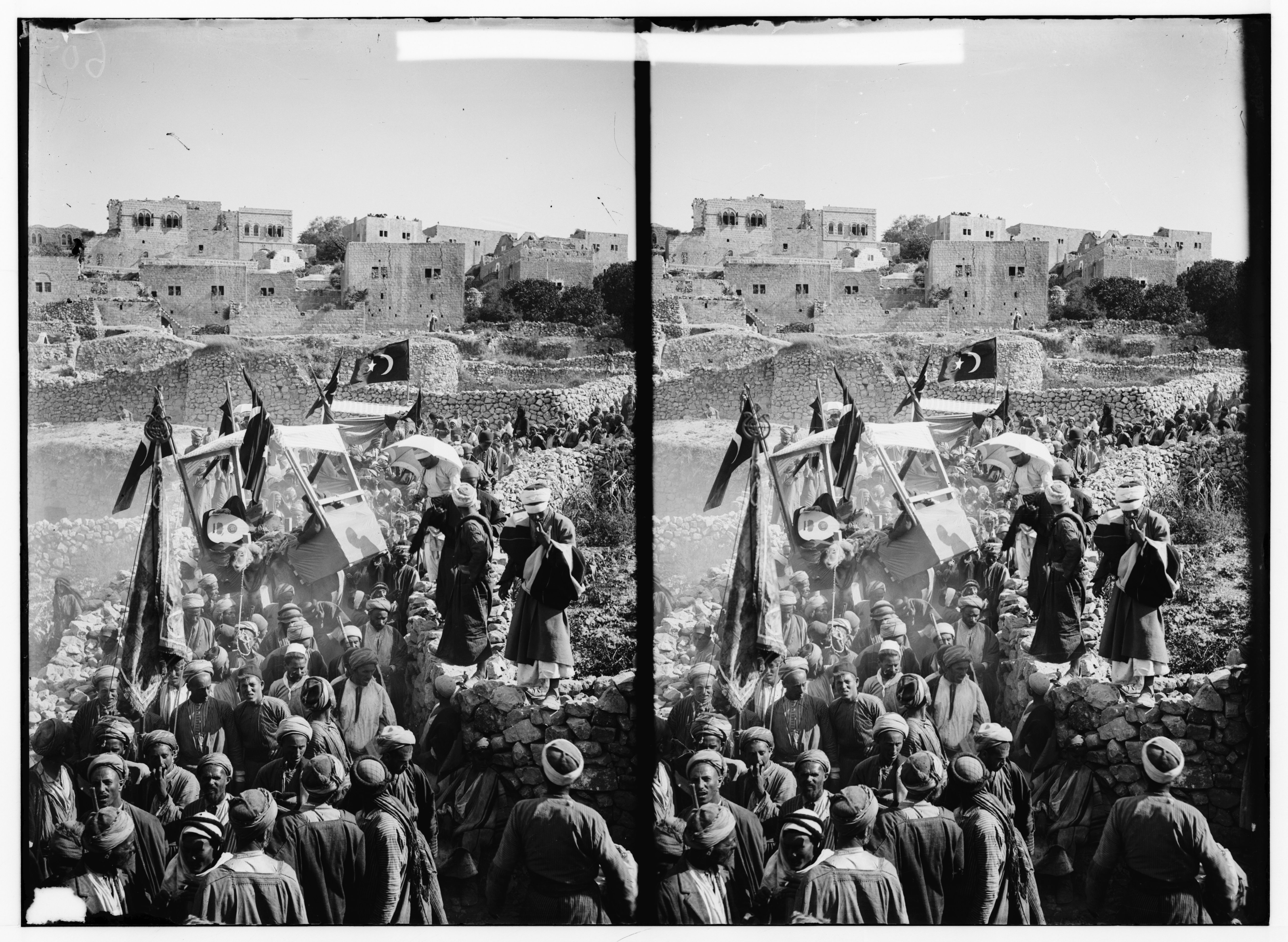 Stereoscopic photograph of a large crowd gathered in front of a building, with flags and a vehicle in the center.