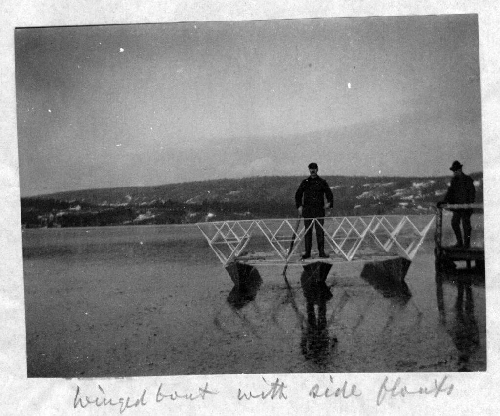 A black and white photograph of a man standing on a geometric metal structure overlooking a hilly landscape.