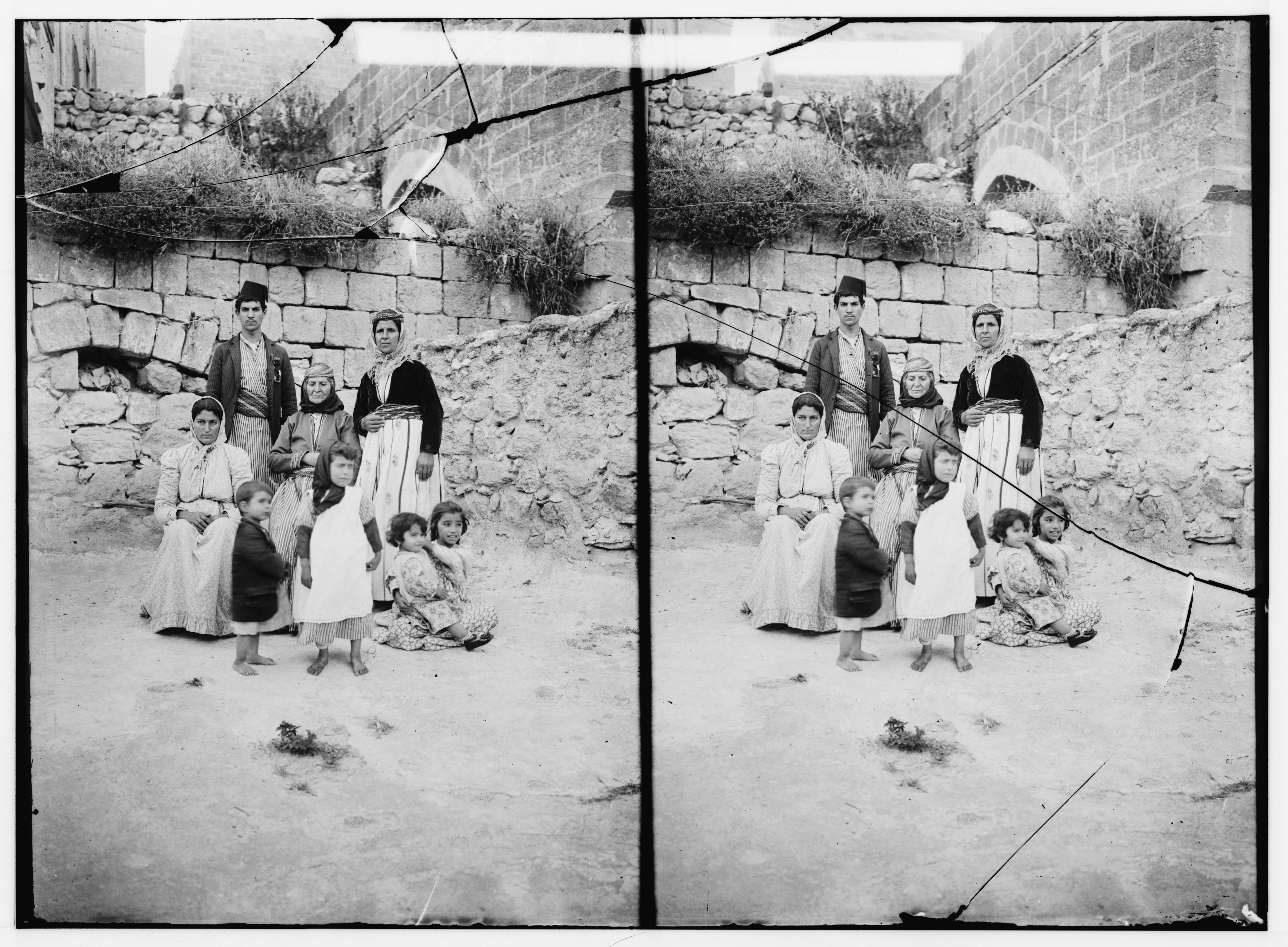 A black and white stereoscopic photograph of a group of people standing in front of a stone wall.