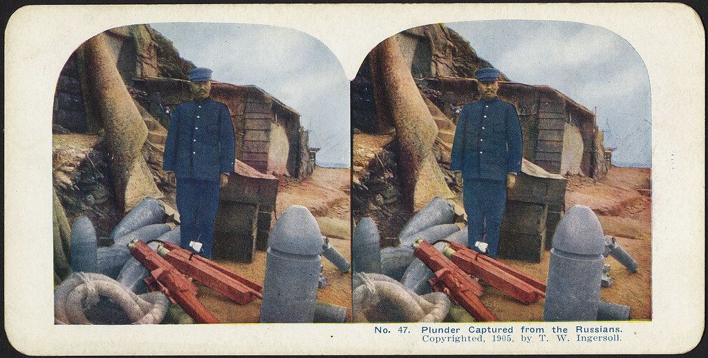 Stereoscopic photograph of a Japanese soldier standing in front of captured Russian artillery during the Russo-Japanese War.