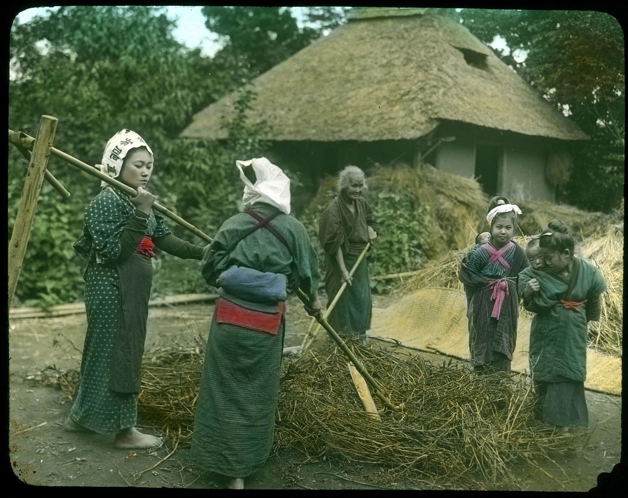 A group of people in traditional Japanese clothing working with straw in front of a thatched-roof building.