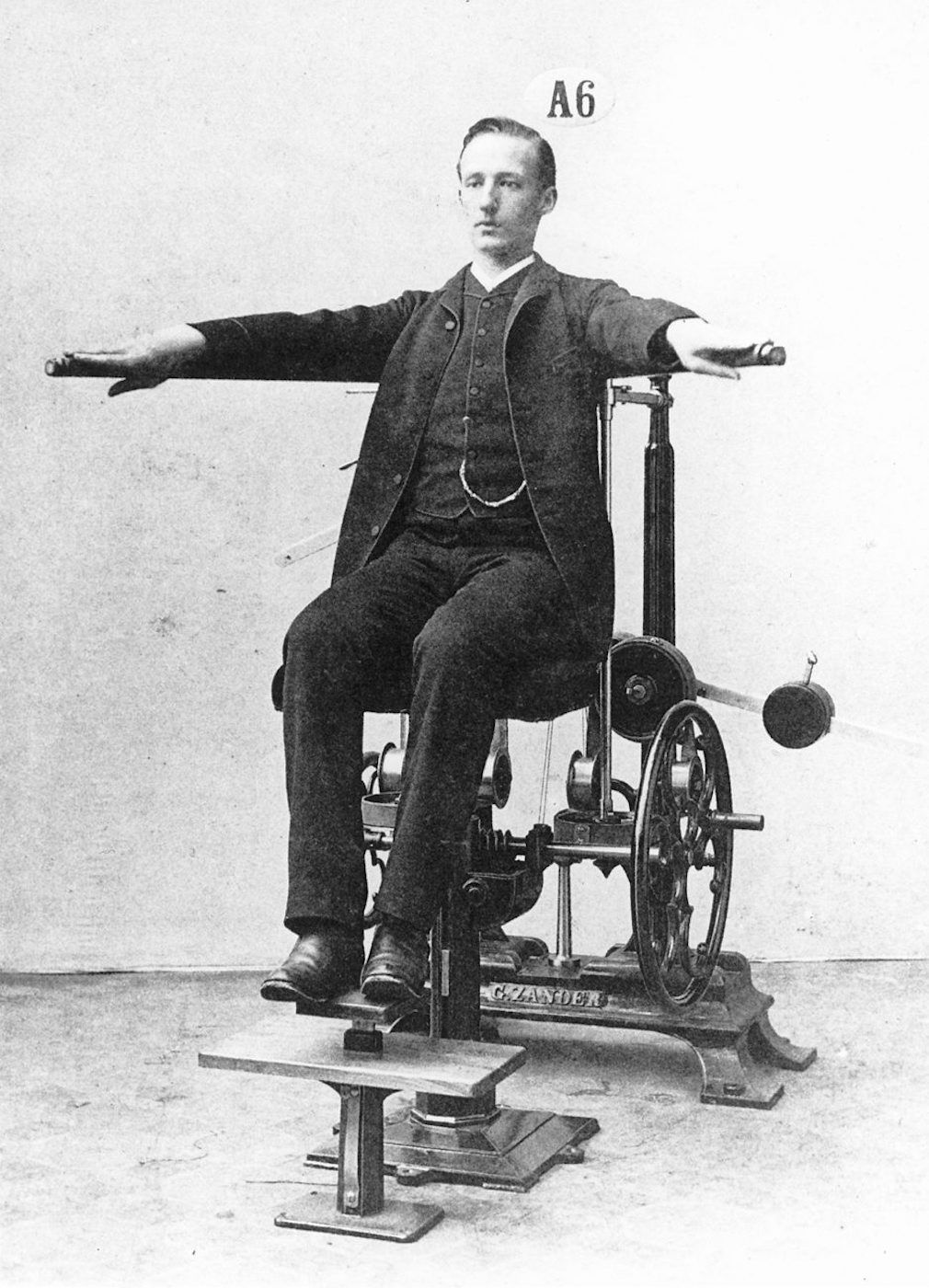 Vintage photograph of a man in formal attire seated in a complex mechanical device.