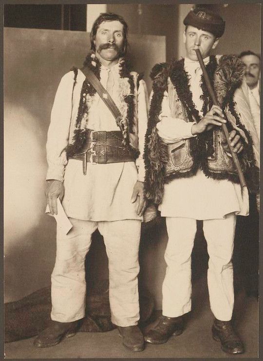 Vintage sepia-toned photograph of two men in traditional attire, one playing a musical instrument.