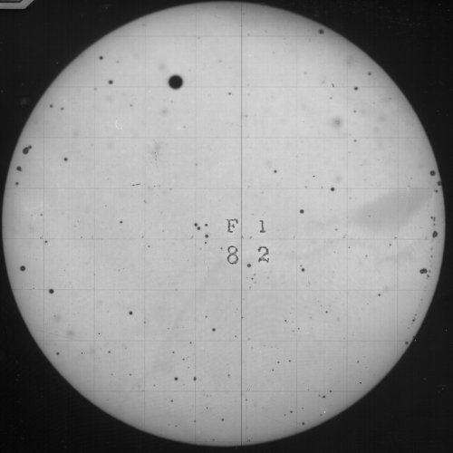A view through a telescope of the sun, showing a prominent sunspot and a grid pattern with text in the center.