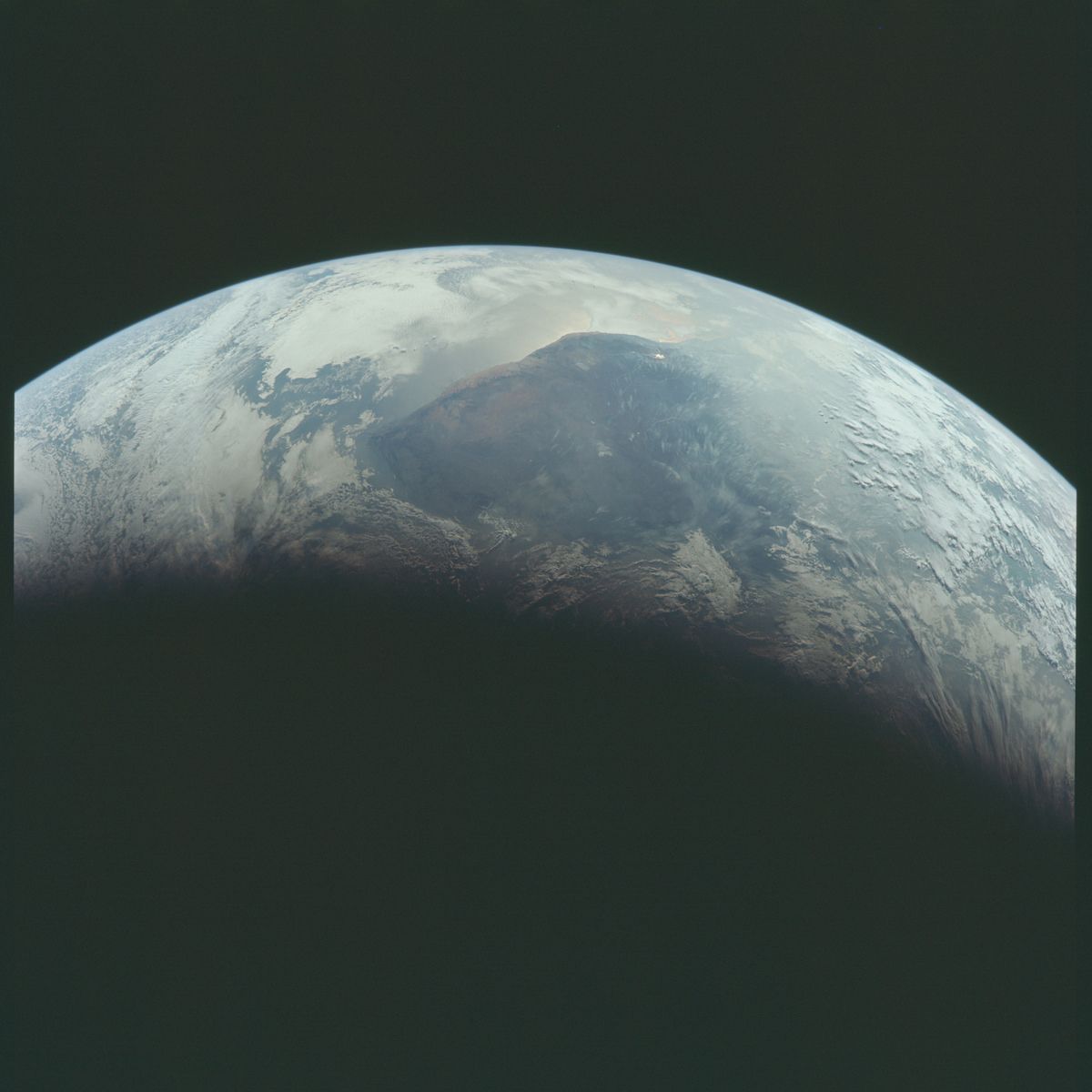 A pale blue-green planet with a dark landmass and a shadowed terminator line.