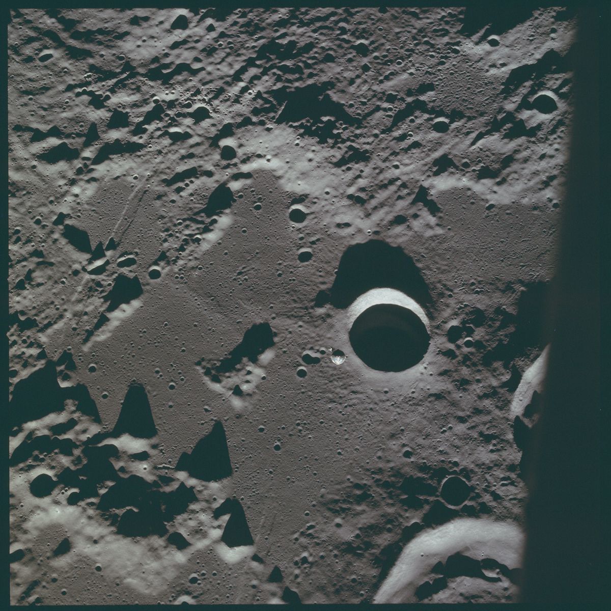 A black and white photograph of a crater on the moon's surface, surrounded by a heavily cratered landscape.