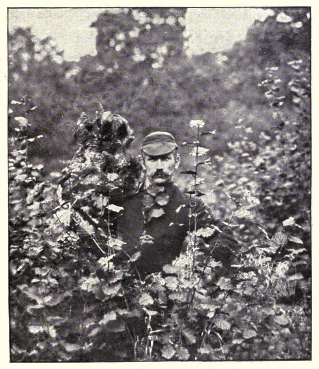 A vintage black and white photograph of a man standing in a dense bush.