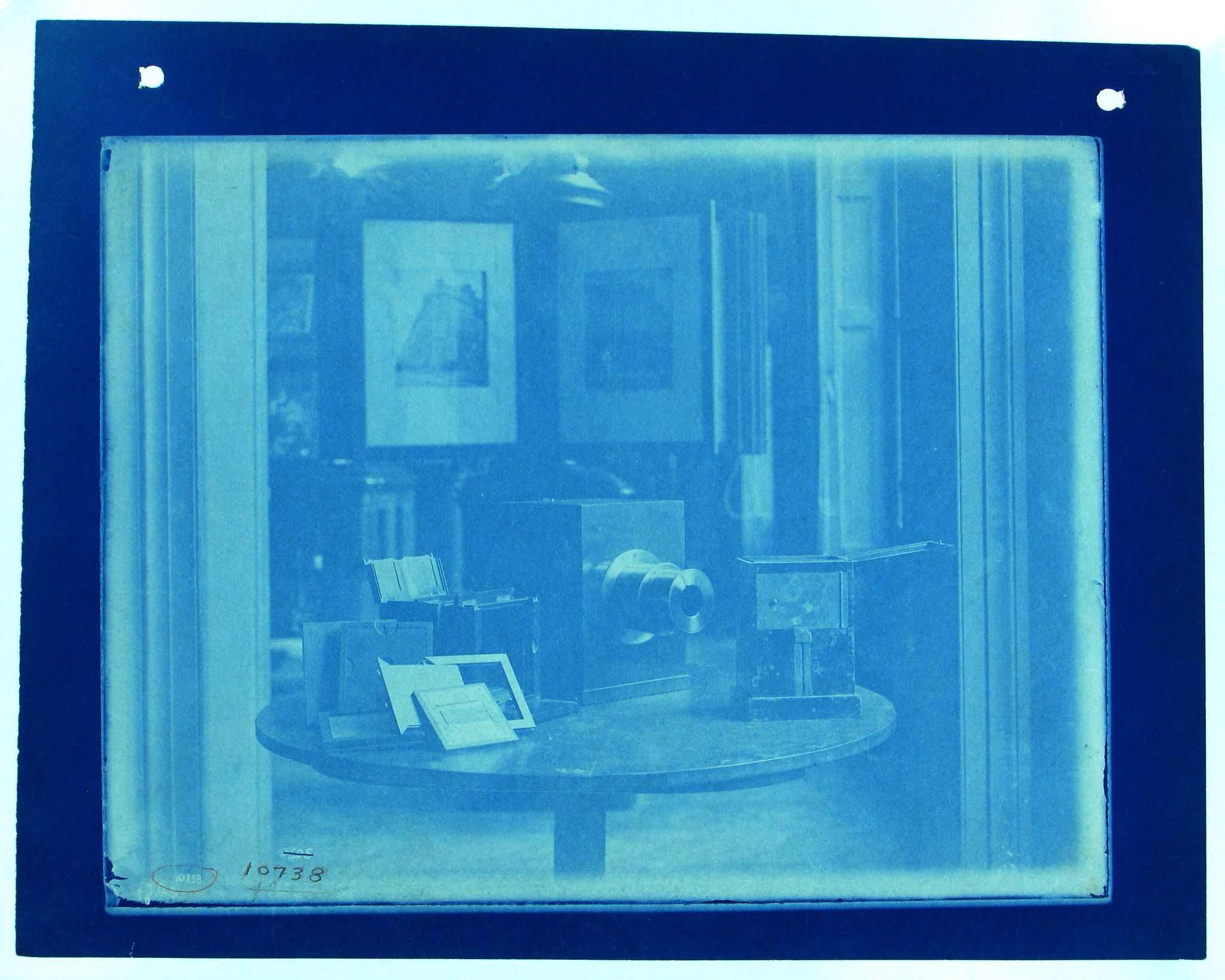 Cyanotype photograph of a room with a round table covered in books and papers.