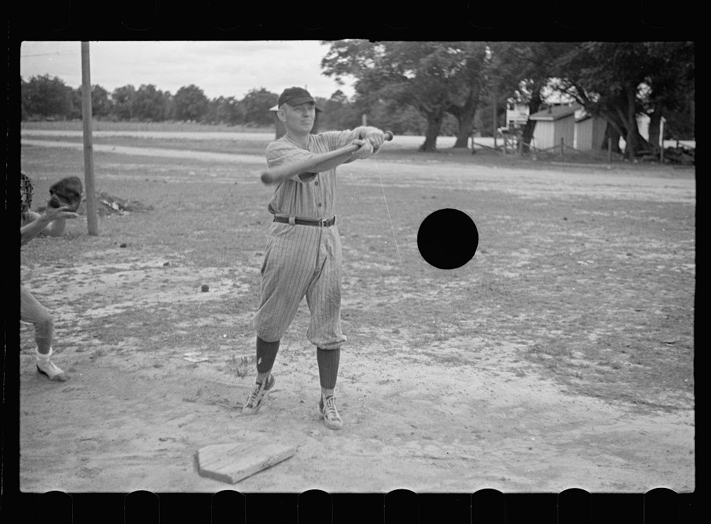 A black and white photograph of a baseball player swinging a bat during a game.
