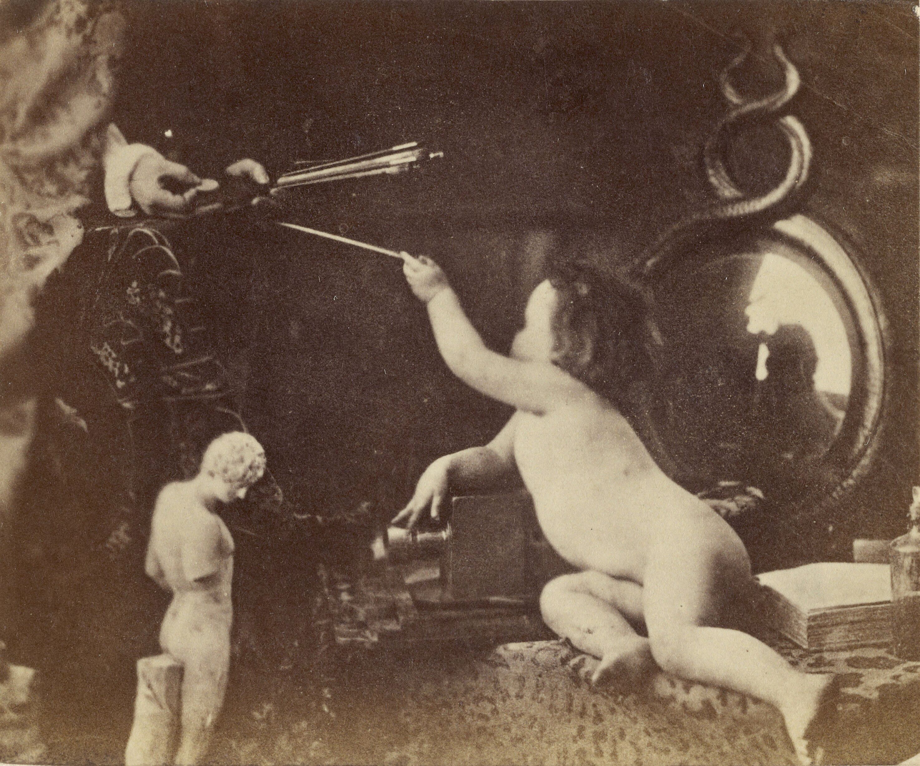 A vintage black and white photograph with a nude male figure aiming a wand at a burst of arrows, with a classical statue and a large machine in the background.