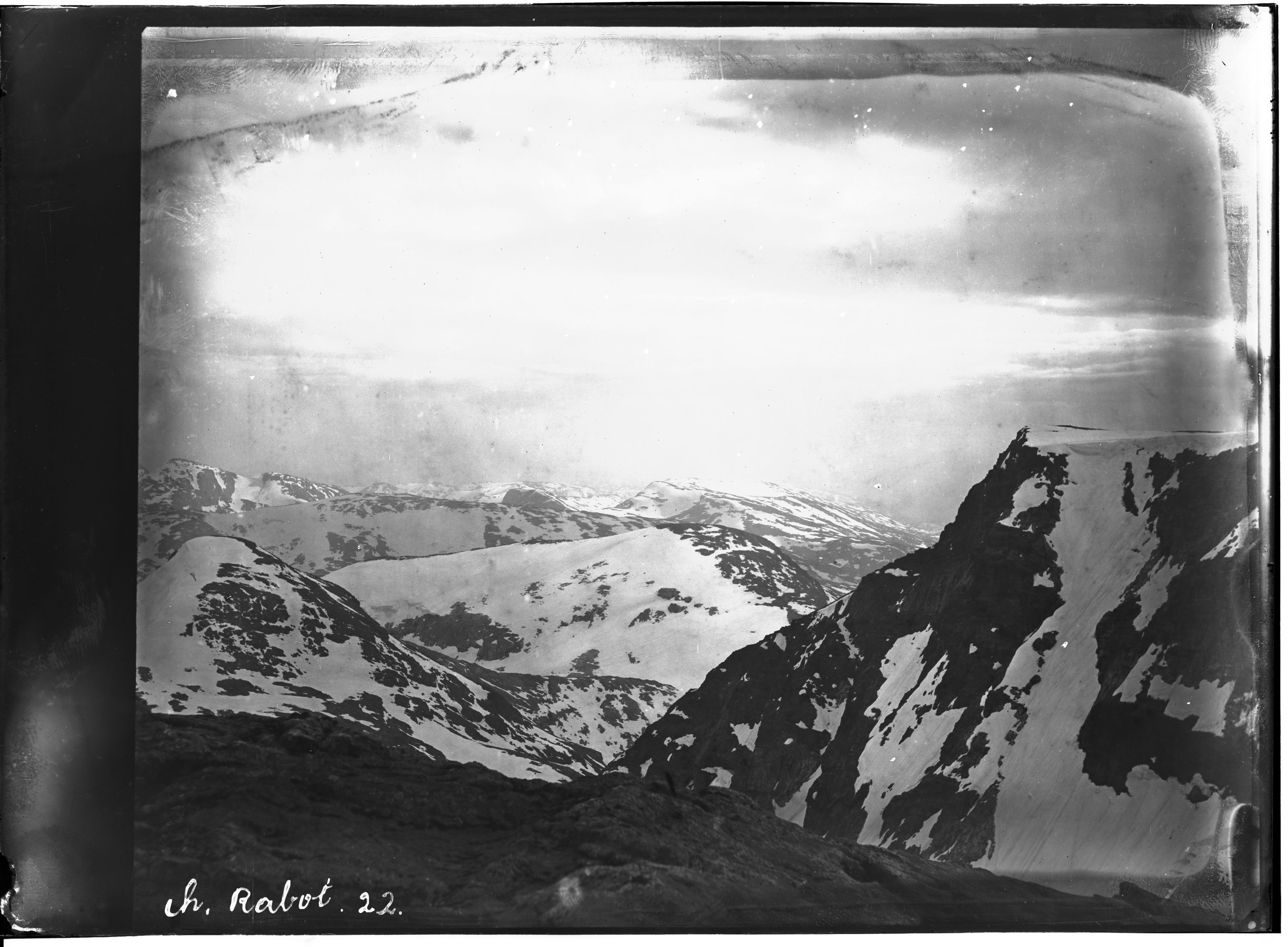 A vintage black and white photograph of a mountainous landscape with snow-covered peaks and a rugged terrain.
