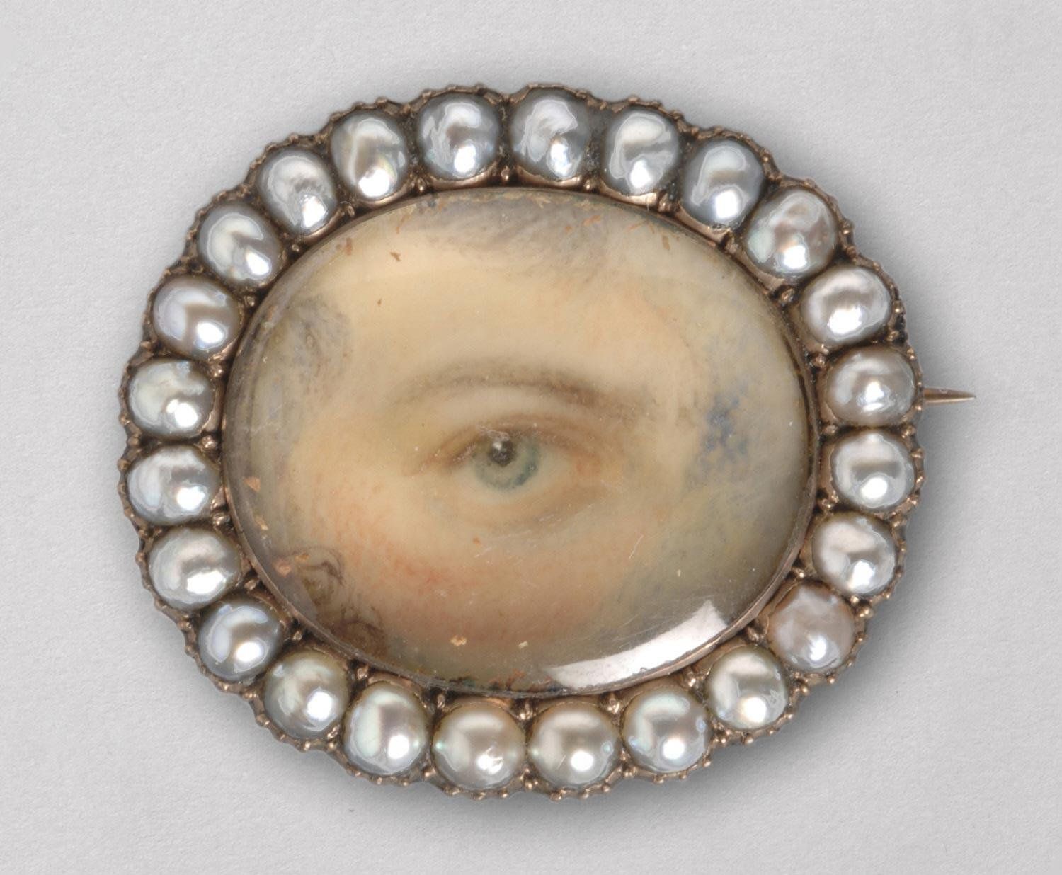 Close-up of a vintage brooch featuring a painted eye surrounded by pearls.