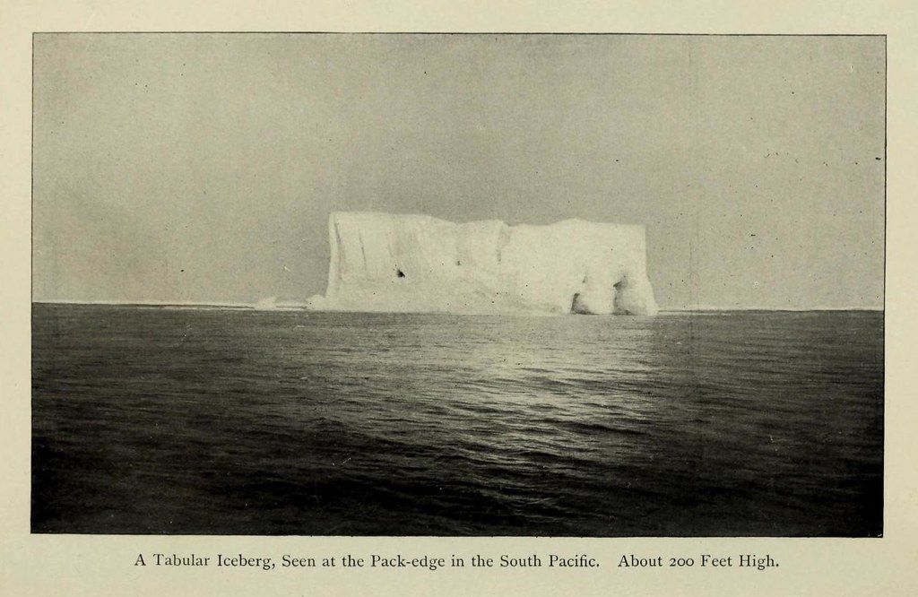 A vintage black and white photograph of a large, tabular iceberg floating in the ocean in the South Pacific.