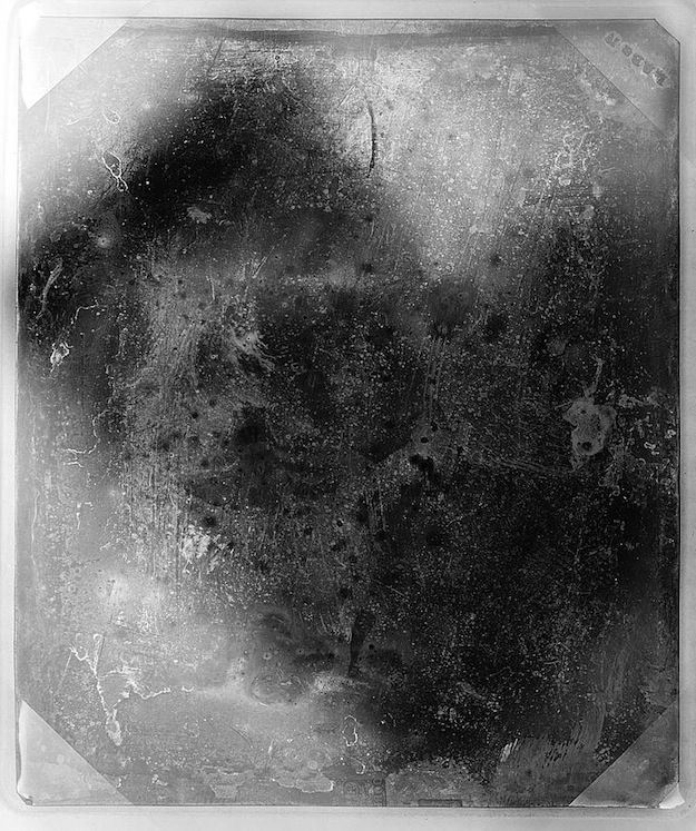 A daguerreotype portrait of a person with dark hair and eyes, wearing a collar and clothing from the 19th century. The image is heavily textured and shows signs of age and wear.