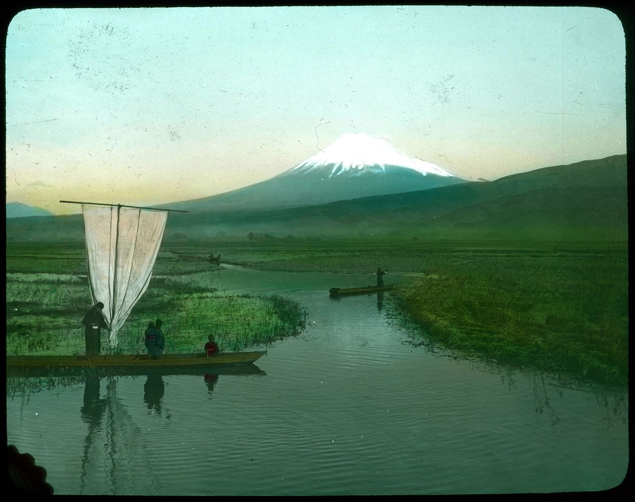 Vintage photograph of a waterway with boats and Mount Fuji in the background.