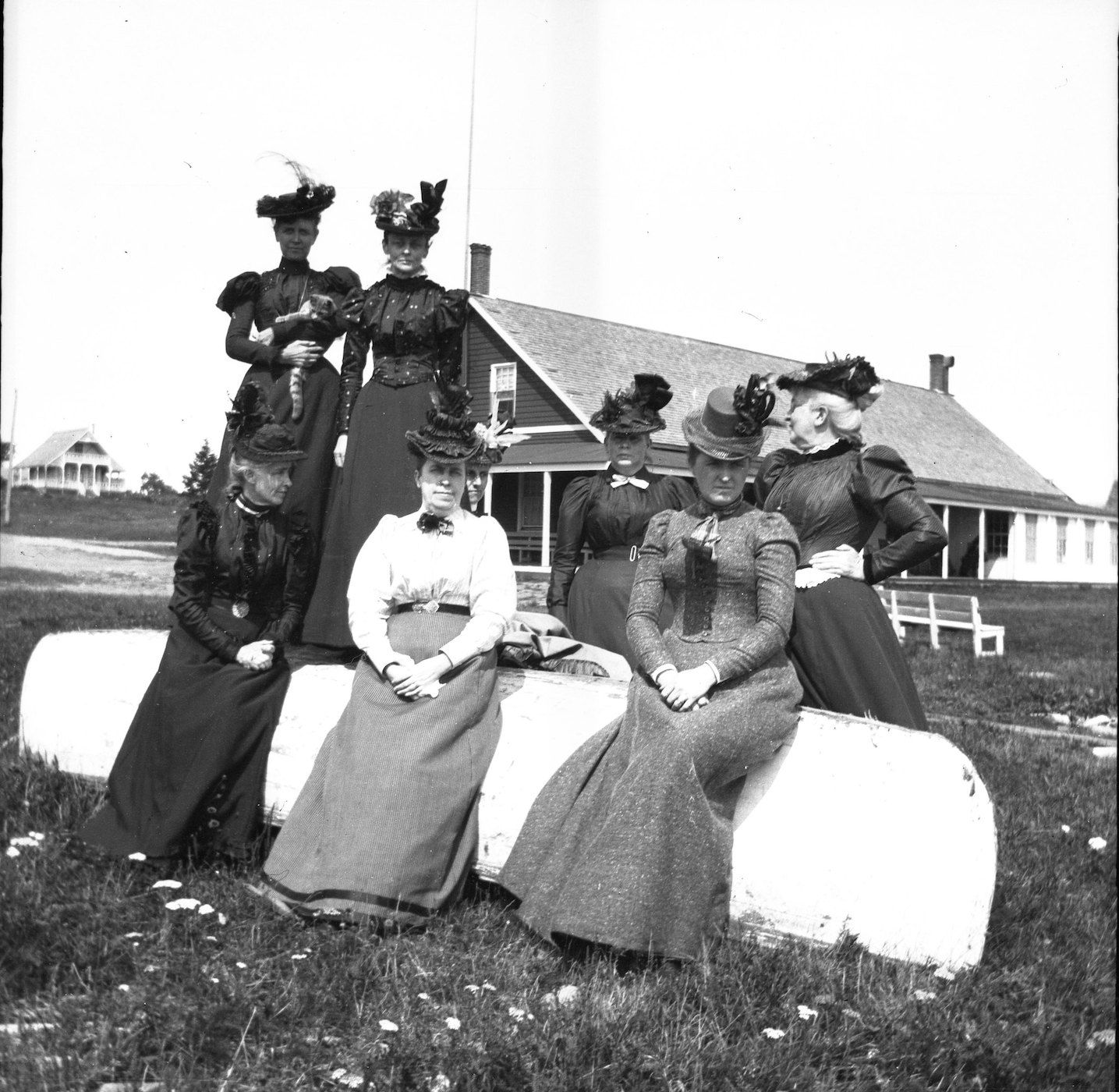 A vintage black and white photograph featuring a group of eight women posing outdoors.