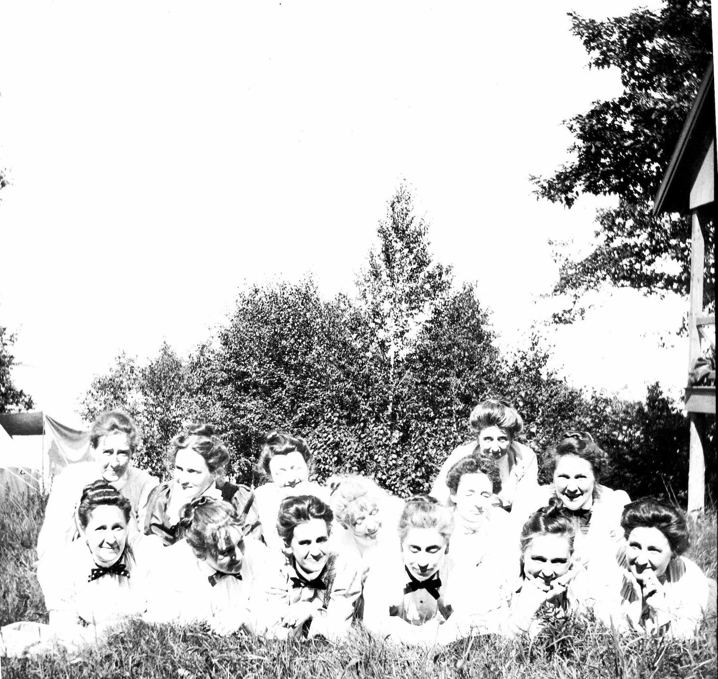 A vintage black and white photograph of a group of young women lying on the grass, looking towards the camera.
