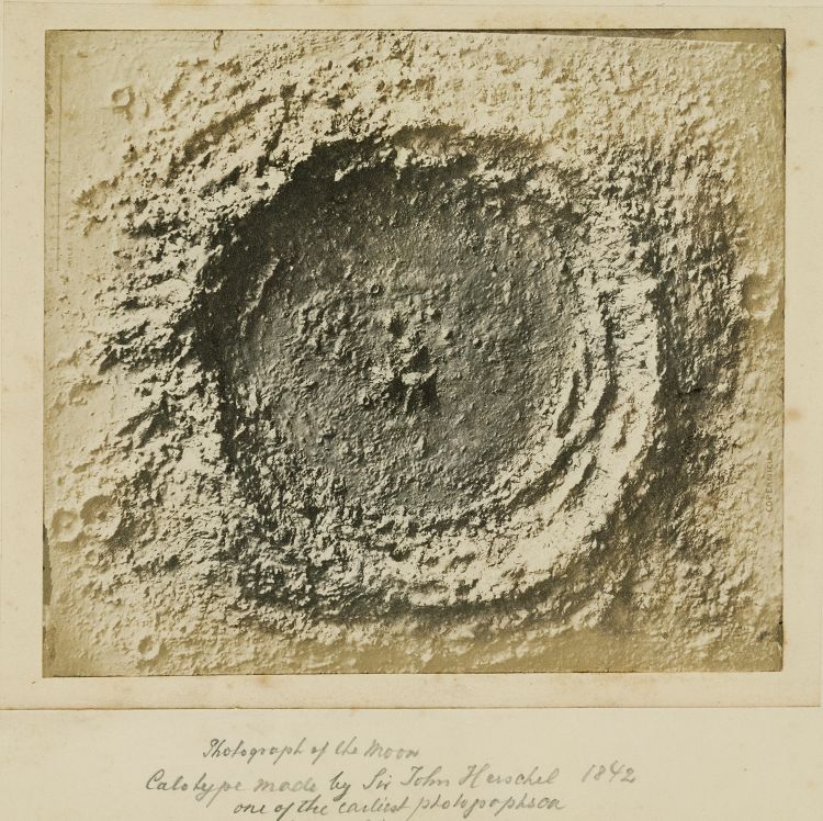 Vintage photograph of a lunar crater taken by Sir John Herschel in 1842, showing a dark, textured depression surrounded by a speckled lunar surface.