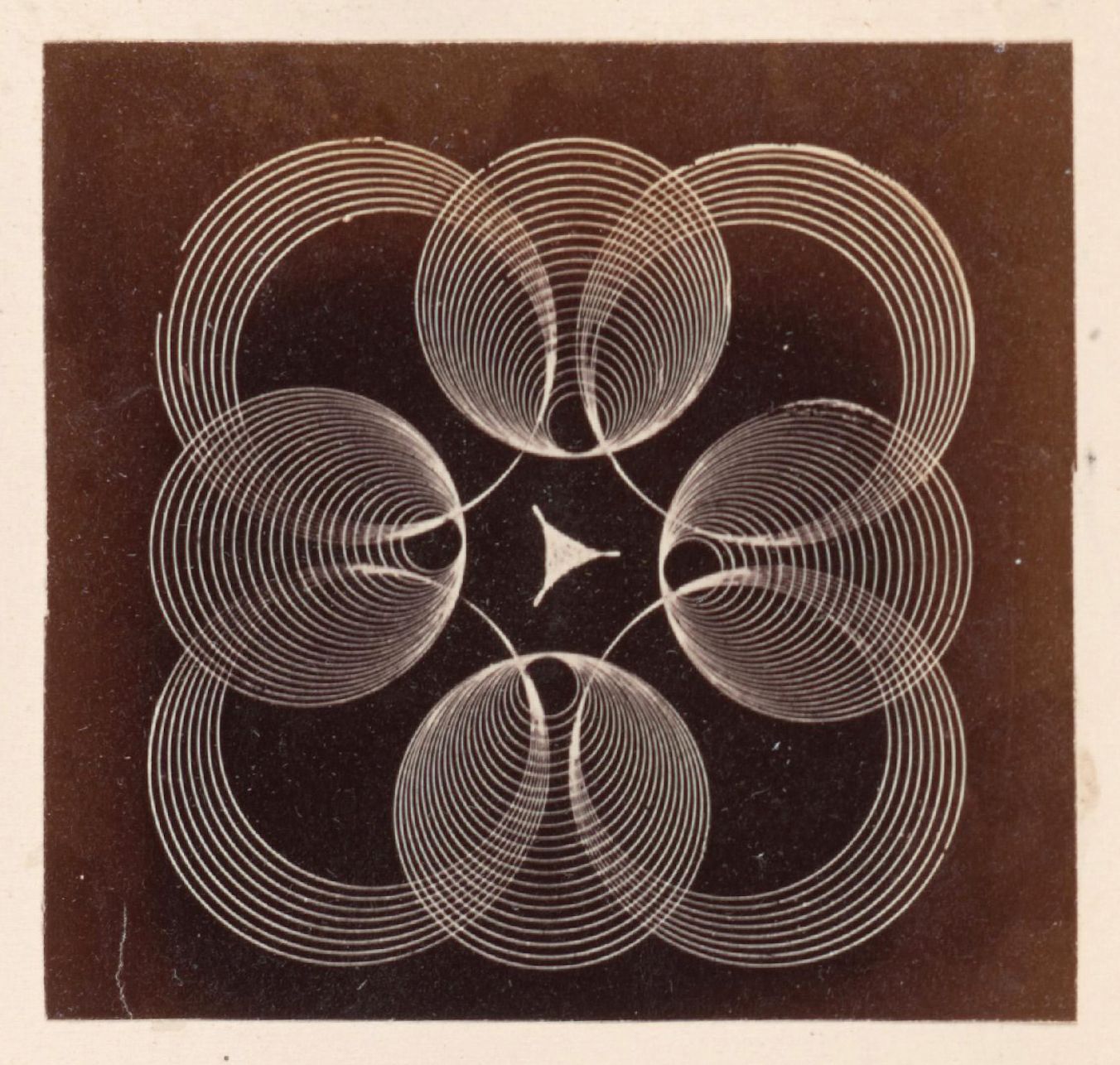 A vintage photograph of a complex geometric pattern with concentric arcs arranged in a flower-like formation, centered around a small triangle.