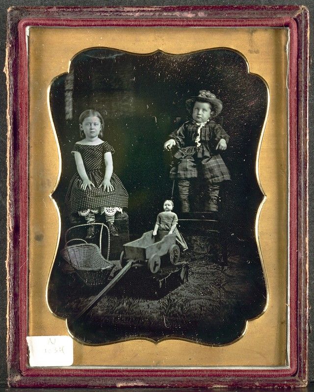 A vintage daguerreotype photograph of two children with toys in a grassy field, encased in an ornate frame.