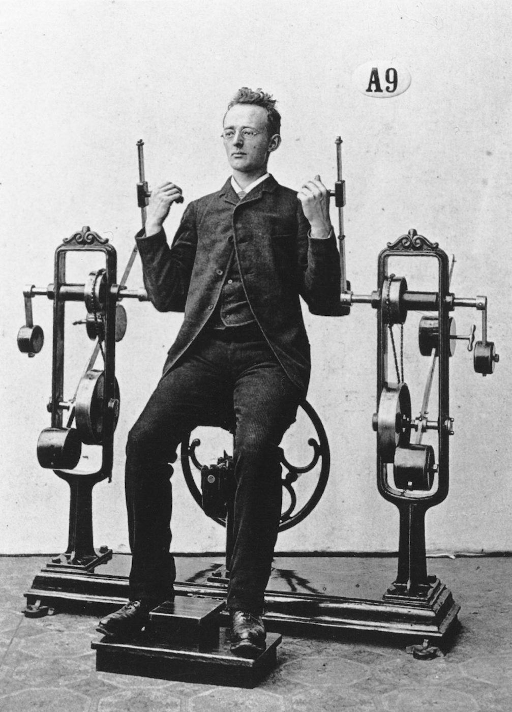 A vintage black and white photograph of a man using a complex exercise machine.