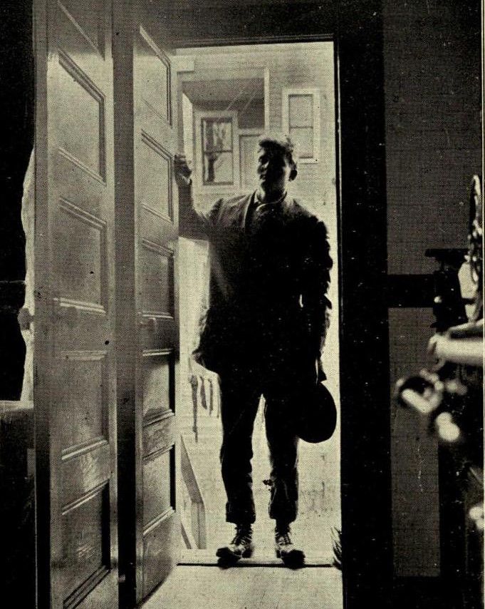 A vintage black and white photograph of a man standing in a doorway.