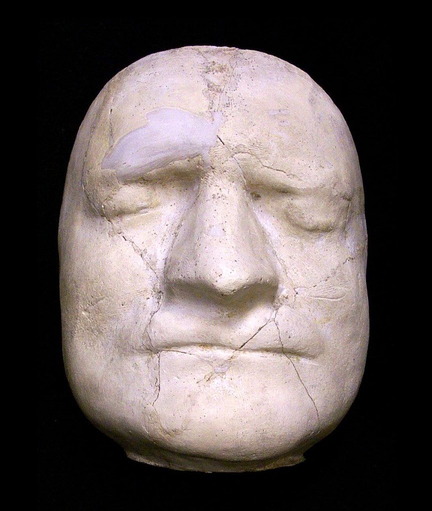 Close-up of a stone sculpture of a human face with closed eyes and a serene expression.