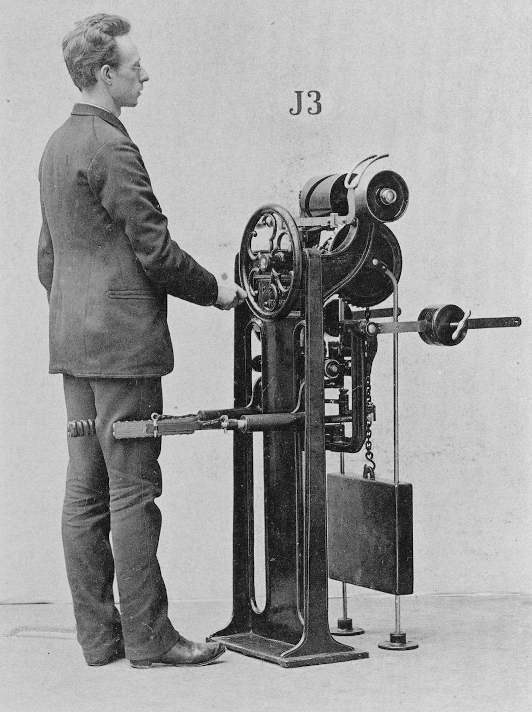 A black and white photograph of a man standing next to a complex machine labeled 'J3'.