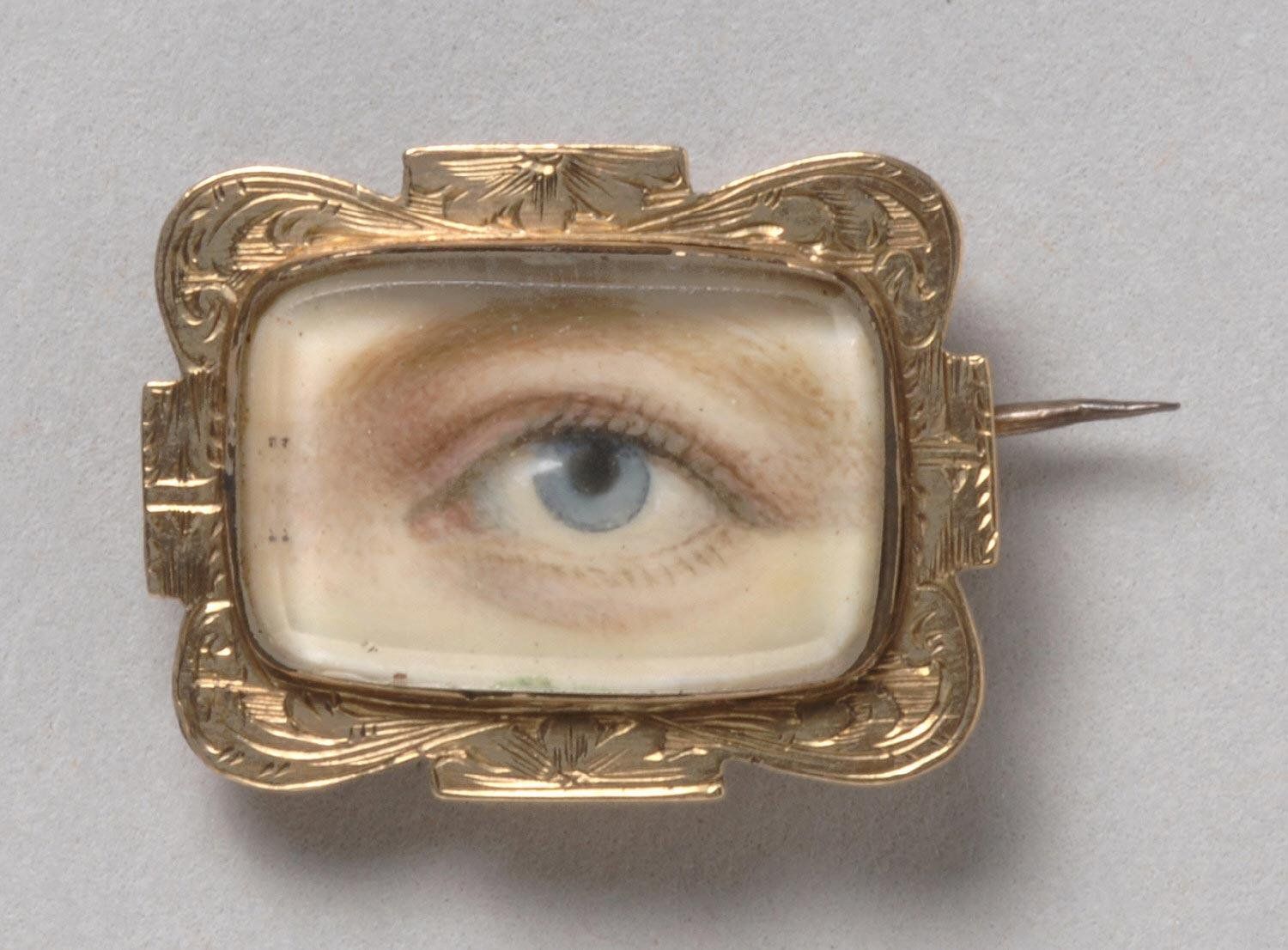 Close-up of a vintage brooch featuring a painted eye set within an ornate gold frame.