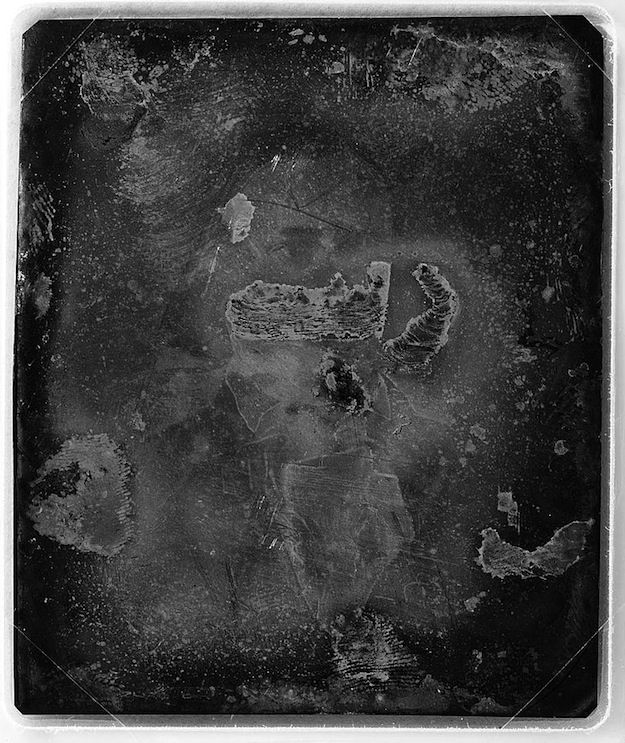A dark, antique portrait of a person wearing a crown and a decorative collar. The image is heavily distressed and has a ghostly appearance.