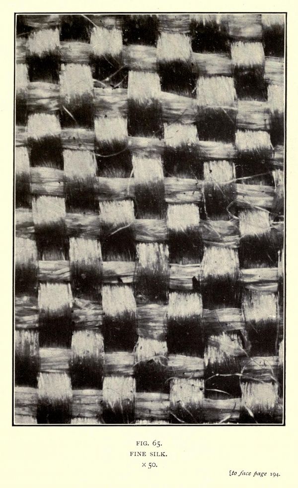 Close-up black and white photograph of a fine silk fabric with a visible weave pattern.