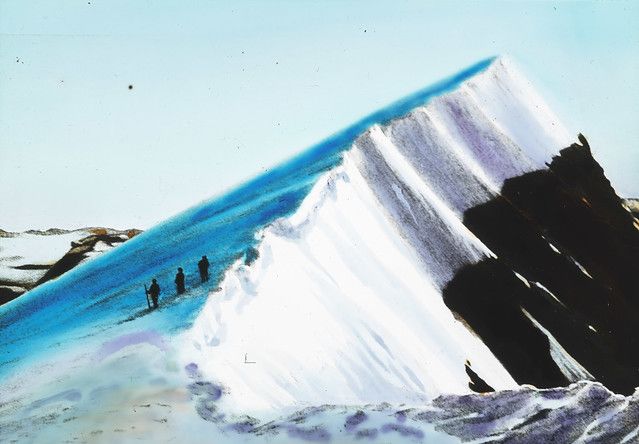 A large blue ice formation with people walking on it, next to a dark cliff, under a pale blue sky.