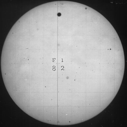 A circular image of the sun with a sunspot and a grid pattern, with numbers and letters in the center.