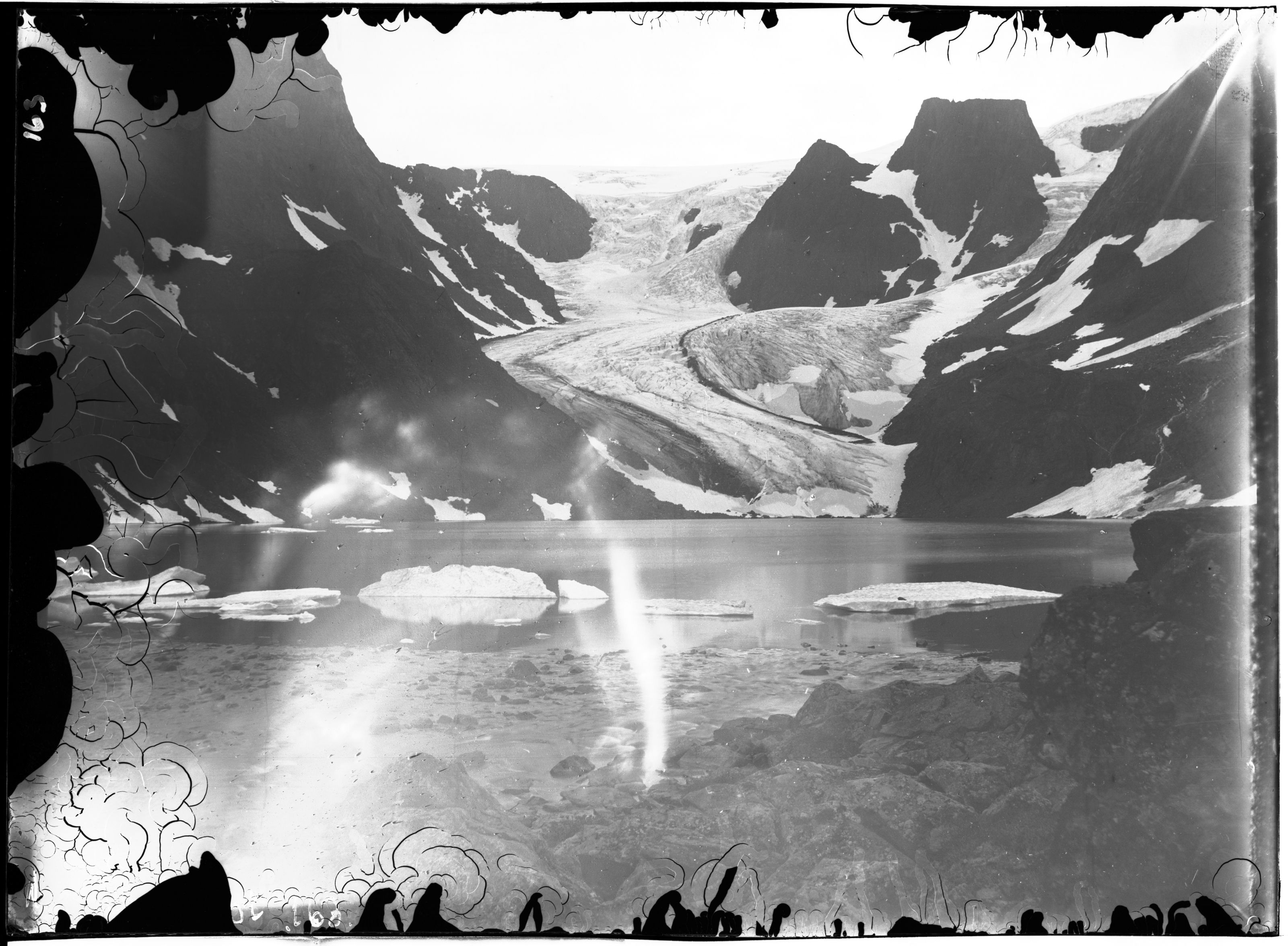 A vintage black and white photograph of a glacial landscape with a serene lake reflecting the surrounding mountains and a distant glacier.