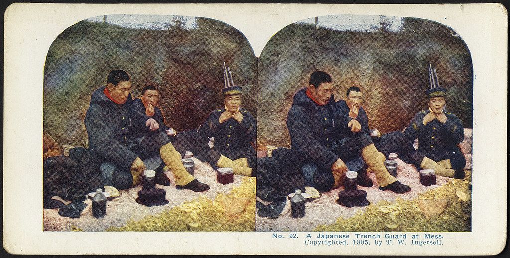 Stereoscope card from 1905 showing five Japanese soldiers in a trench eating a meal.