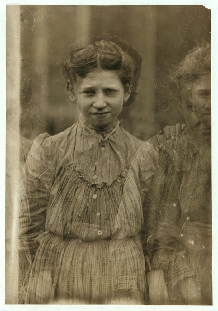 A sepia-toned photograph of a young girl in a striped dress, with two other children partially visible in the background.