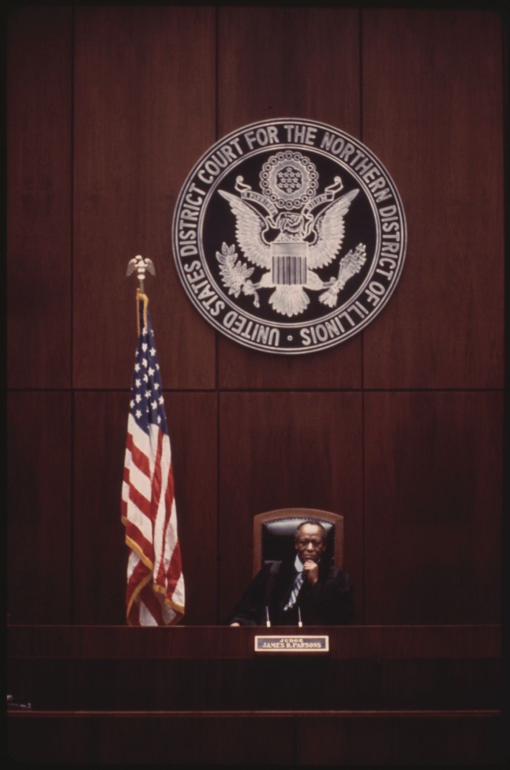 A courtroom scene featuring a judge seated behind a bench with the US District Court seal and an American flag.