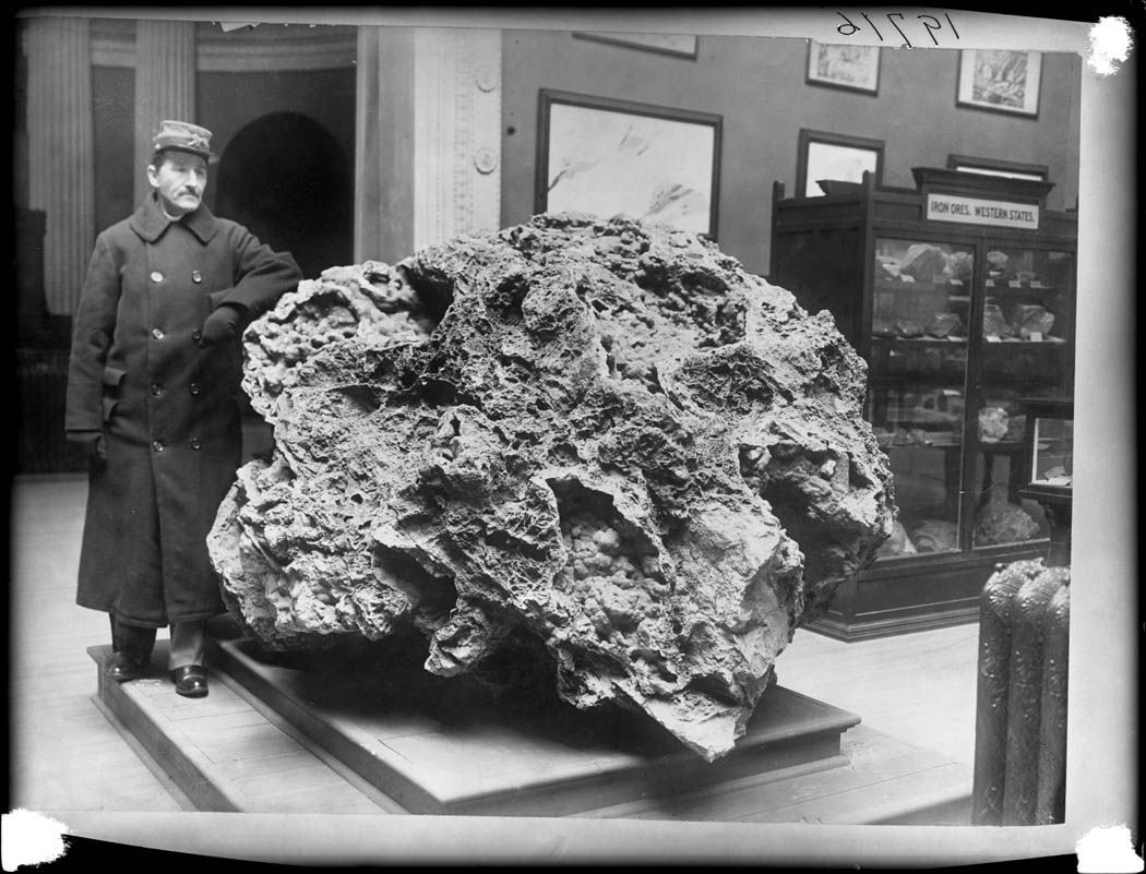 A black and white photograph of a man standing next to a large meteorite in a museum.
