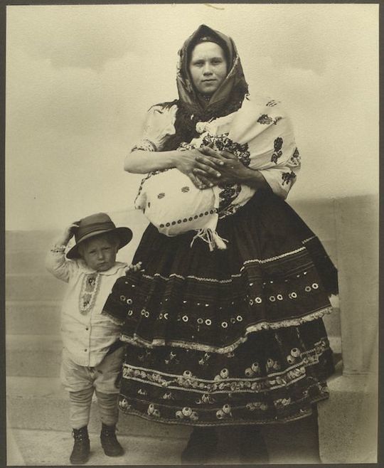A vintage black and white photograph of a woman in traditional clothing holding a baby and standing with a young boy.