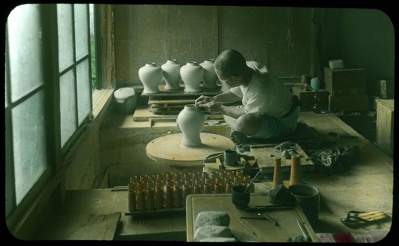A vintage photograph of a potter working at a wheel in a dimly lit workshop.