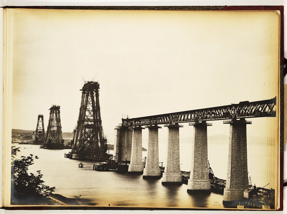 Vintage black and white photograph of the construction of a large railway bridge with numerous stone pillars and scaffolding.