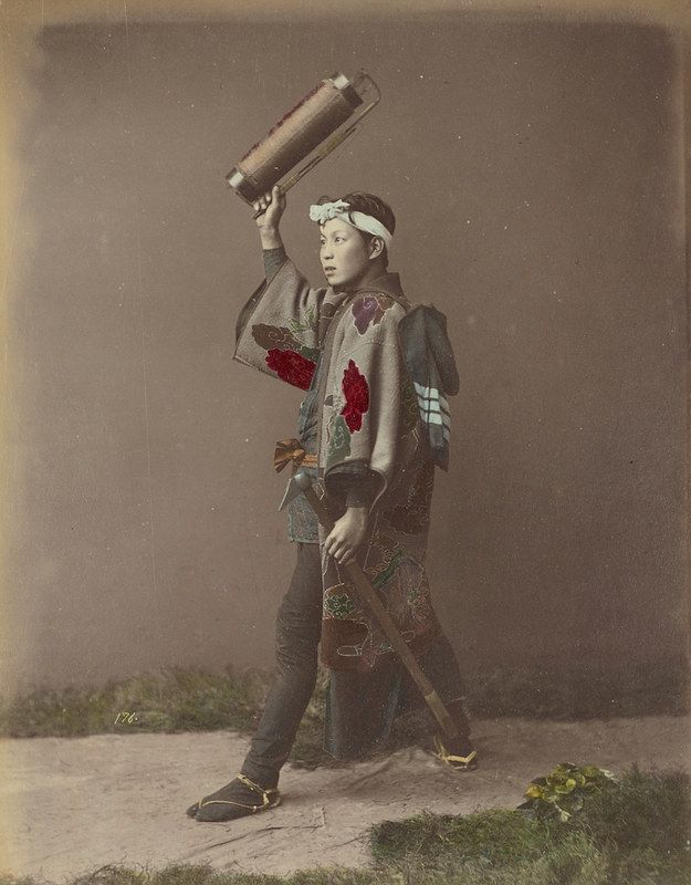 Vintage photograph of a young Japanese boy in traditional clothing holding a cylindrical object above his head.