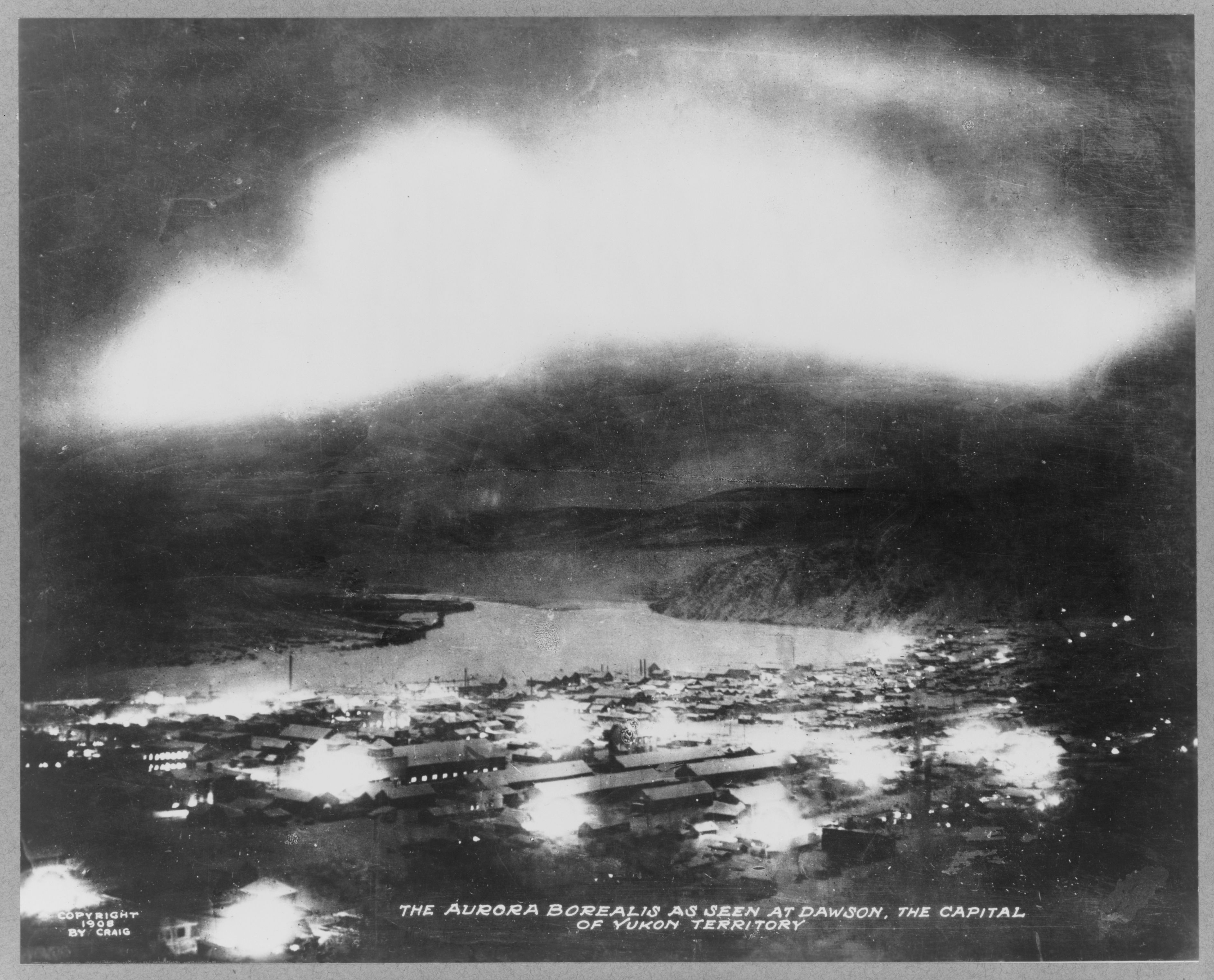 A vintage black and white photograph of the Aurora Borealis over the town of Dawson in the Yukon Territory.