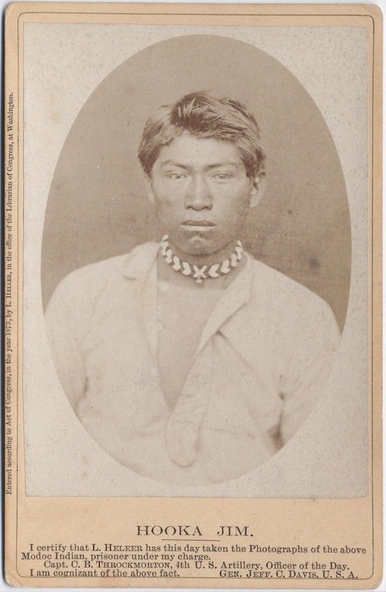 Sepia-toned photograph of a Native American man named Hooka Jim, wearing a white collared shirt and a beaded necklace. The photograph is accompanied by a certification statement identifying him as a Modoc Indian prisoner.